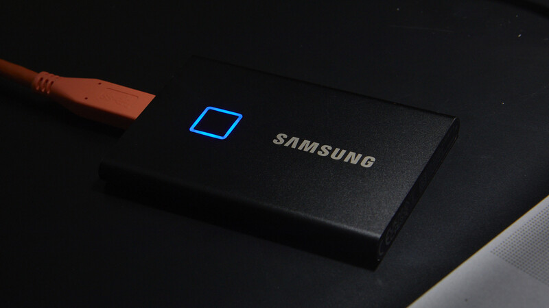 Samsung portable SSD with blue illuminated icon and attached USB-C cable on dark surface.