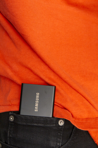 Samsung SSD storage device positioned on black denim against bright orange fabric.