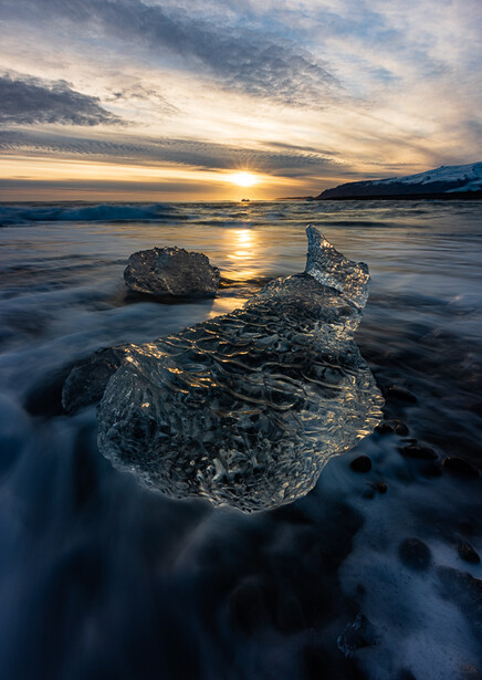 Icebergs washed ashore during golden hour sunset with mountains in the background.