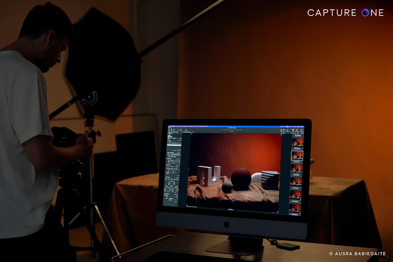 Photographer adjusting a large reflector while reviewing product photography on a monitor displaying editing software.