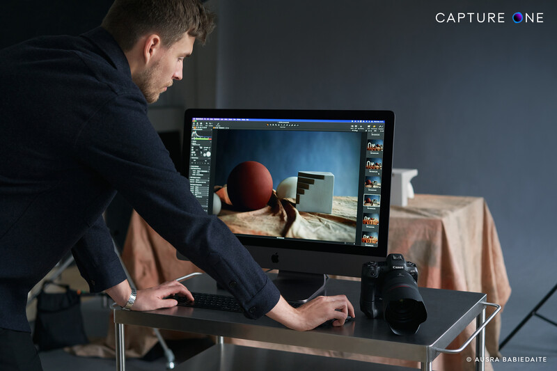 Photographer working at a desktop computer displaying a still life image with spherical objects and fabric in post-processing software.