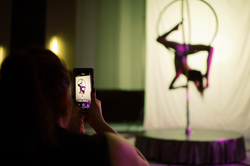 Spectator filming aerial circus performer on silks with smartphone during stage performance.