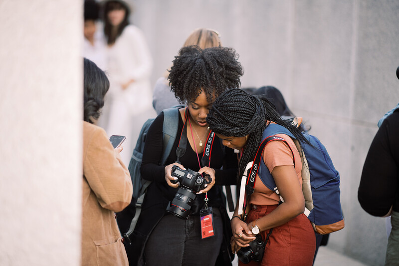 Female photographers review images on a camera at an indoor event or conference.