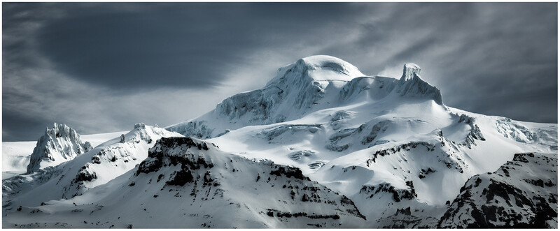 Snow-covered mountain peaks with dramatic storm clouds overhead and exposed dark rock formations.