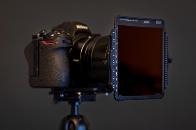 Professional camera with attached external monitor mounted on tripod against gray background.