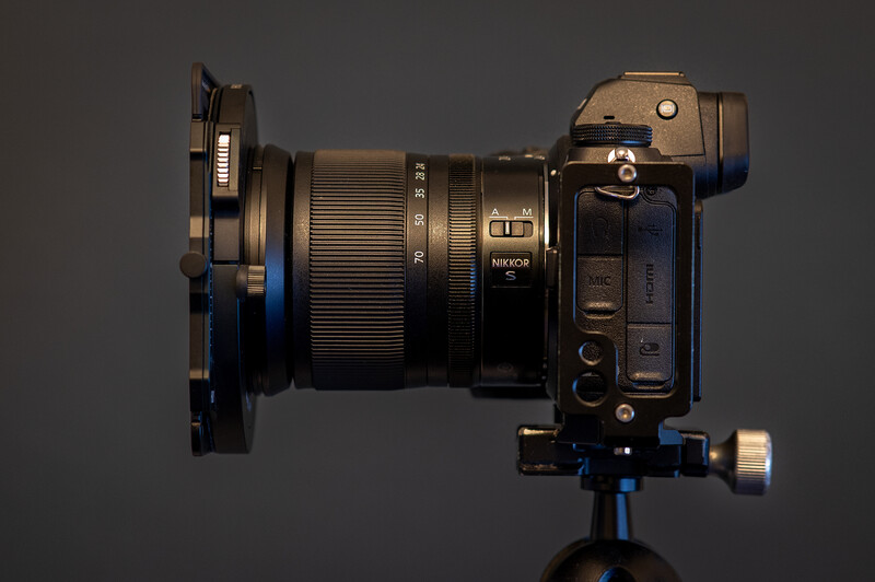 Nikon mirrorless camera with telephoto lens mounted on blue tripod head, viewed from above against gray background.