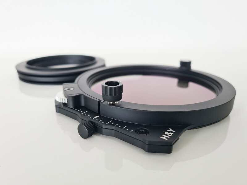 Black circular filter holder with adjustment knob and measurement markings on a white surface.