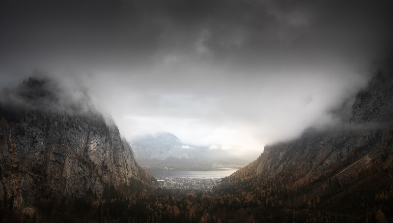 Alpine valley framed by steep forested mountainsides under dramatic storm clouds.
