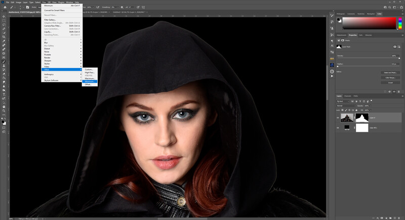 Portrait of a woman with reddish hair wearing a black hood against a dark background.