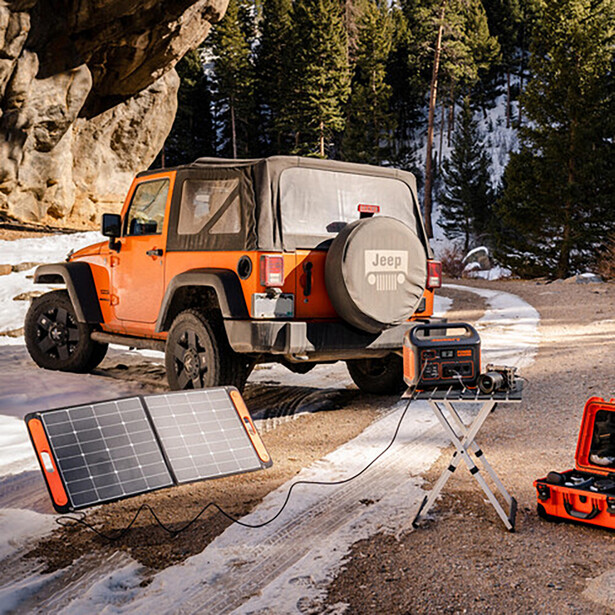 Orange Jeep with solar panel and portable power station setup in a rocky canyon landscape.
