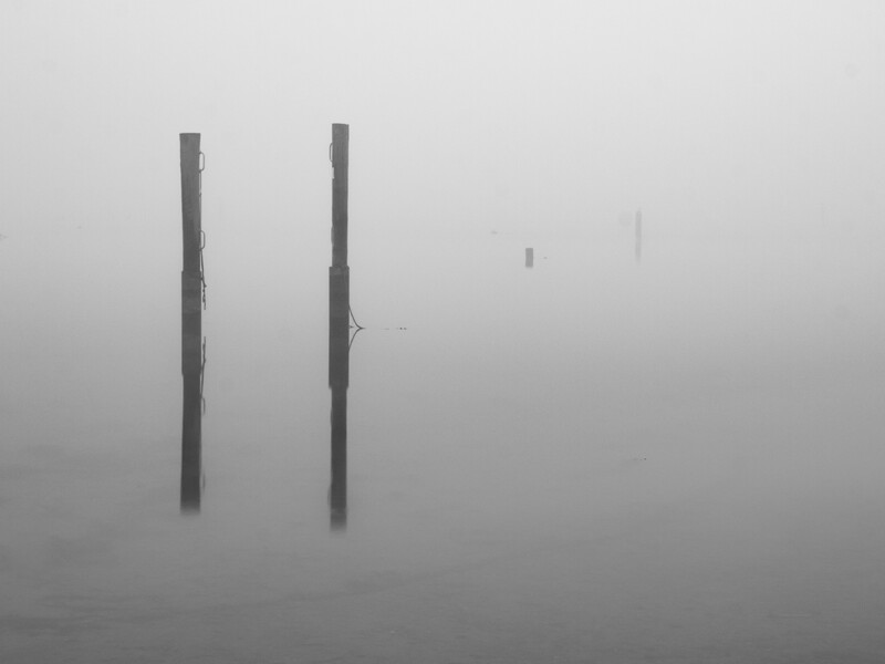 Two weathered wooden posts emerging from dense fog over calm water.