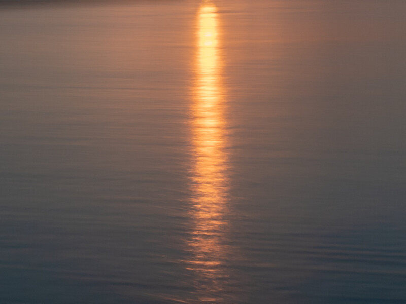 Golden sunlight reflecting vertically across calm water at sunset or sunrise.