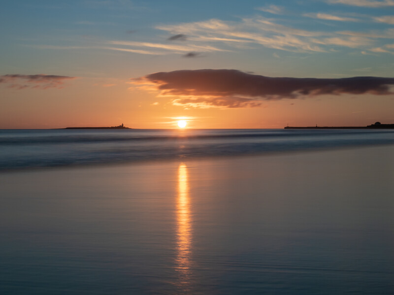 Sun setting over calm water with golden light reflecting on the ocean surface.