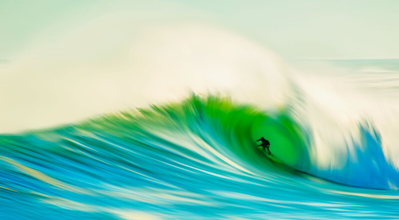 Surfer riding inside a barrel of a large turquoise wave with white spray and foam.