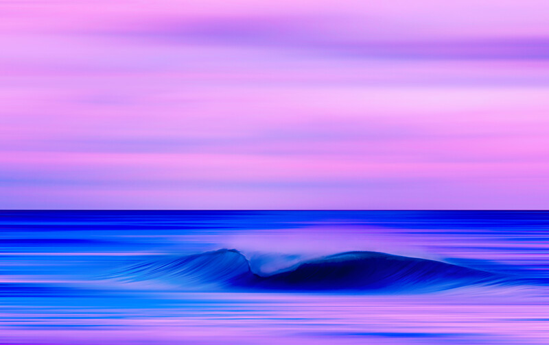 Ocean wave at twilight with vibrant pink and blue sky reflected in water.