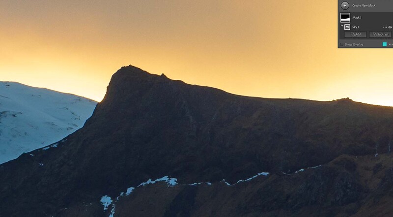 Silhouetted rocky mountain peak against golden sunset sky with snowy slopes visible on the left.