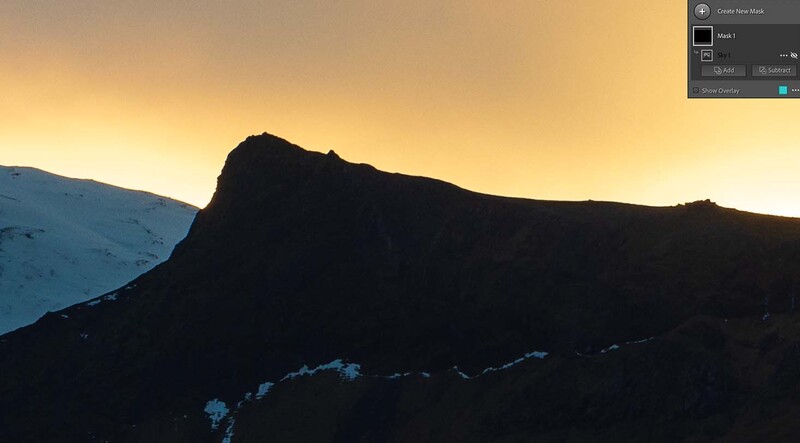 Silhouetted mountain peak against golden sunrise sky with snow-covered slopes.