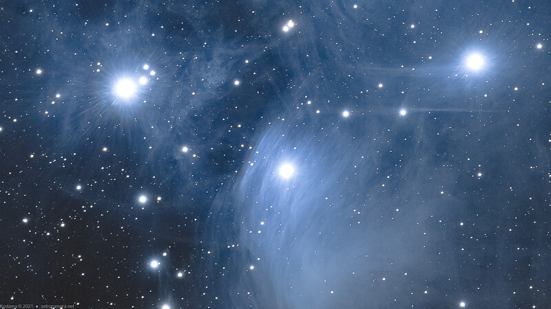 Pleiades star cluster with bright blue stars surrounded by wispy nebulosity against a dark starfield.