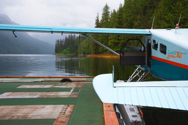 Floatplane docked at a remote alpine lake surrounded by evergreen forest and mountains.
