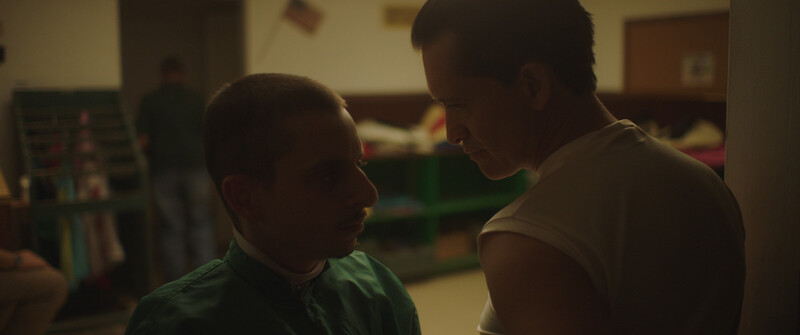 Two people in conversation inside a classroom or community space with warm indoor lighting.