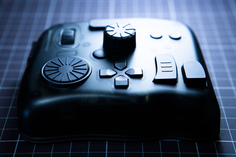 Close-up of a black game controller with raised buttons and controls against a blue grid background.
