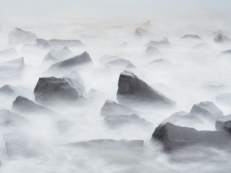 Rocks partially submerged in flowing ocean waves creating a misty, ethereal seascape.