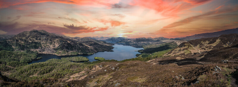 Alpine lake surrounded by forested mountains under a dramatic sunset sky with orange and pink clouds.