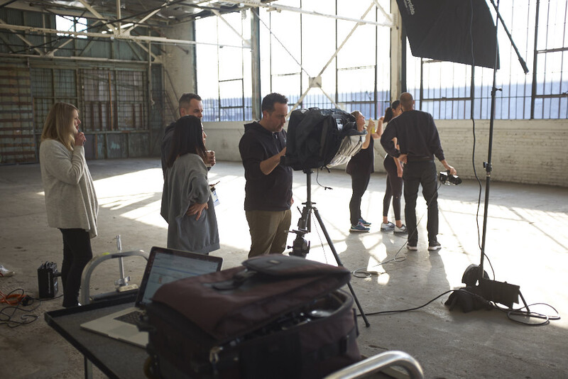 Behind-the-scenes view of a film or photo production in an industrial studio space with crew members operating camera equipment.