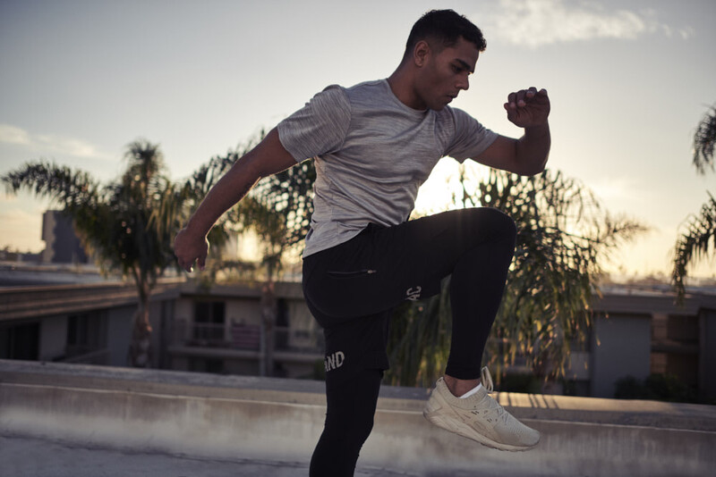 Male athlete performing a high knee exercise on an urban rooftop at dusk.