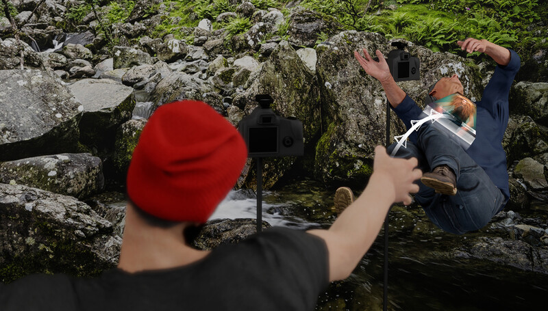 Photographer in red beanie capturing a shot of a person climbing moss-covered rocks near water.