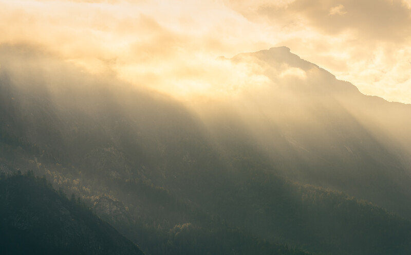 Mountain peak silhouetted against golden sunlight breaking through layered clouds and mist.