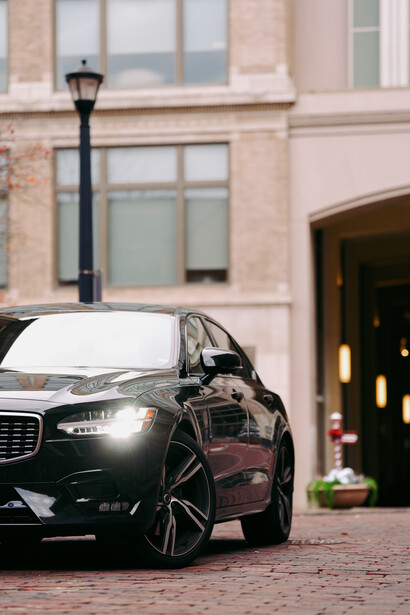 Black luxury sedan parked in front of a brick building entrance with an open driver's door.