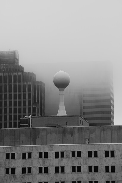 Spherical water tower rising above downtown buildings shrouded in dense fog.