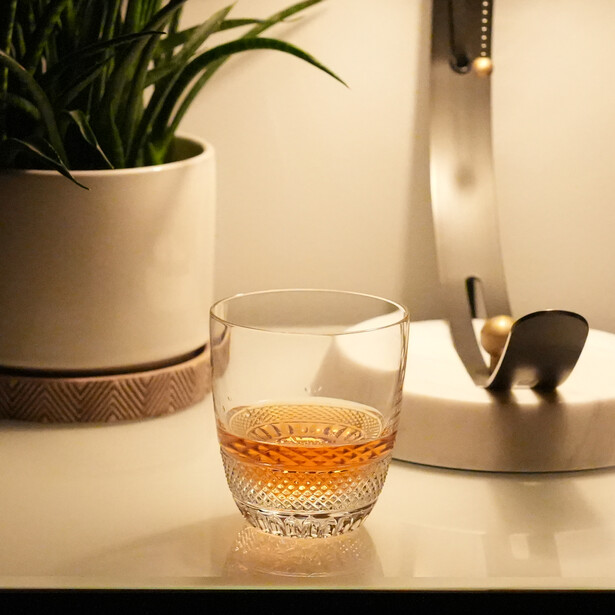 Glass of amber liquid on a bright surface with potted plant and desk accessories in soft natural light.