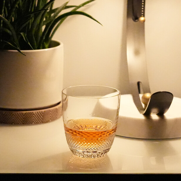 Glass of amber liquid on a minimalist desk with warm sunlight streaming across white surfaces.