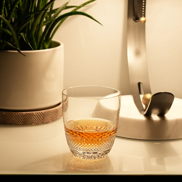 Glass of amber liquid on a minimalist desktop with potted plant and desk accessories.