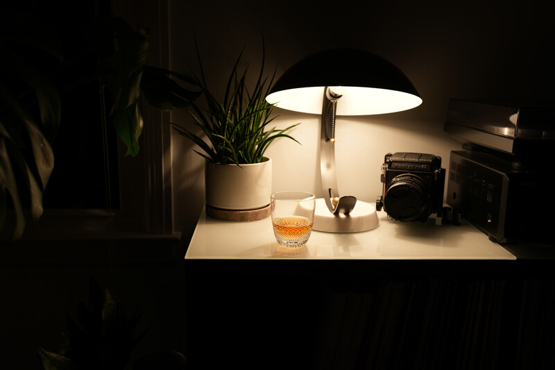 Minimalist desk setup lit by overhead lamp, featuring potted plant, glass of water, and vintage camera.