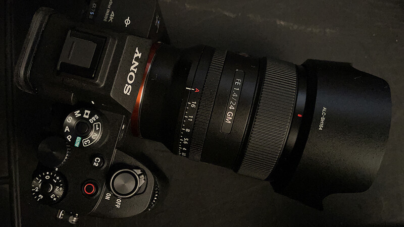 Sony mirrorless camera with attached telephoto lens and lens hood on dark surface.