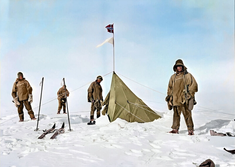 Five explorers in tan parkas stand around a canvas tent with a flag on a snow-covered landscape.