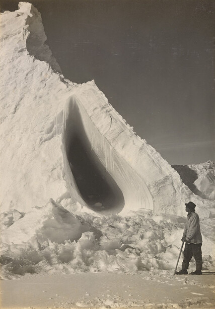 Man standing before massive white chalk cliff formation with deep erosion cavity.