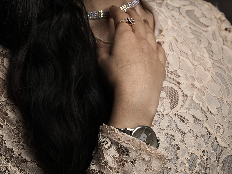 Woman's hand wearing rings and watch resting on delicate white lace fabric in warm, directional light.