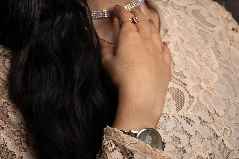Woman's hand wearing jewelry resting on lace fabric with watch visible.