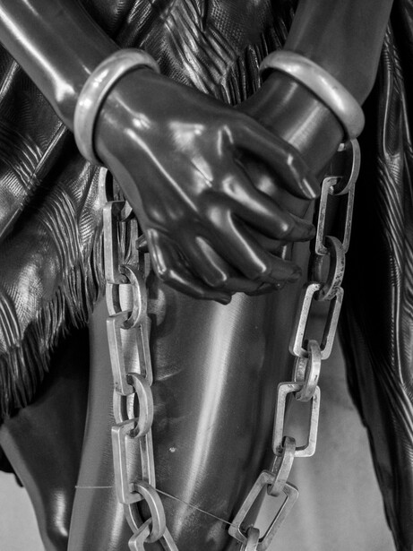 Black and white close-up of a gloved hand gripping a heavy chain wrapped around a muscular leg.