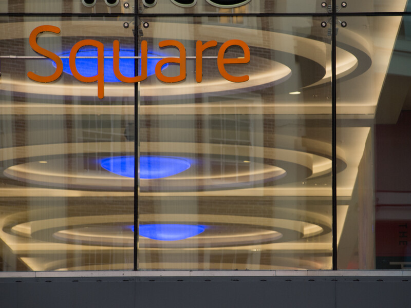 Glass storefront window displaying orange and blue neon signage with geometric lighting design.