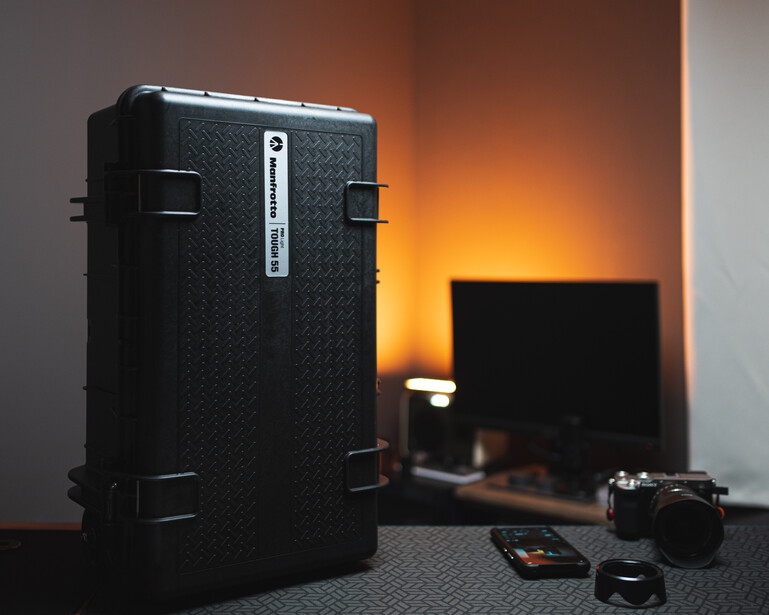 Large black protective equipment case next to a camera and lens on a desk with warm orange lighting.