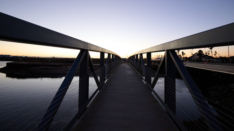 Long footbridge extending into twilight with symmetrical railings and calm water below.