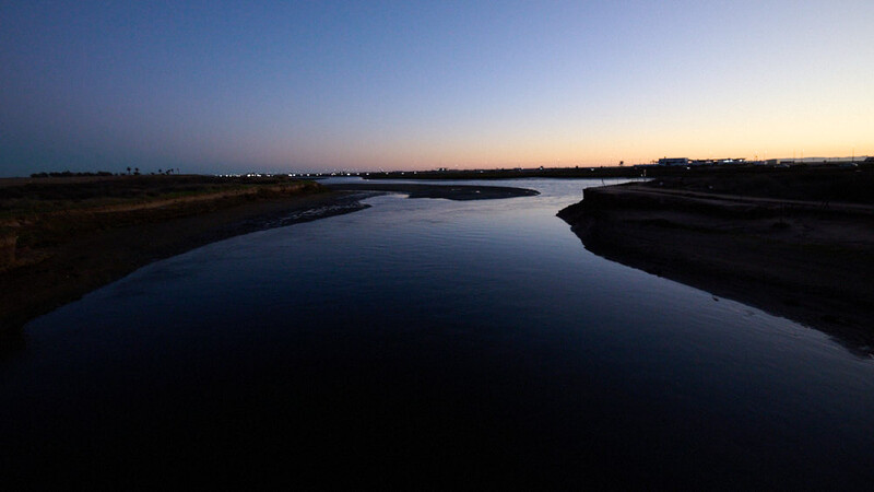 A winding river reflects the twilight sky at dusk, bordered by dark marshland on both banks.
