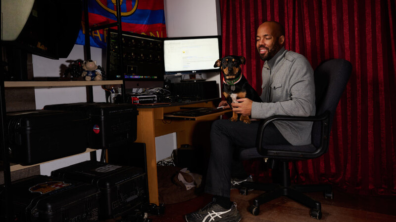 Man seated at desk holding a dog while working at a computer setup with dual monitors.