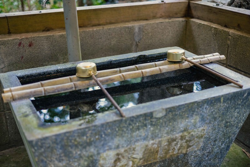 Traditional Japanese stone water basin with bamboo spout and dipper in filtered natural light.