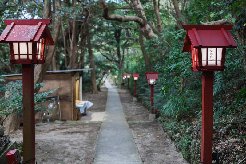 Red wooden lantern posts line a tree-canopied pathway with stone steps.